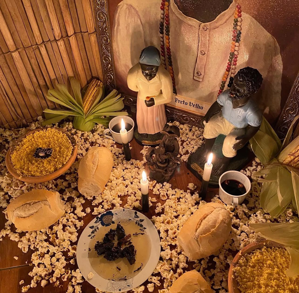 Altar espiritual com Preto Velho, velas acesas, oferendas de milho, pipoca e pão